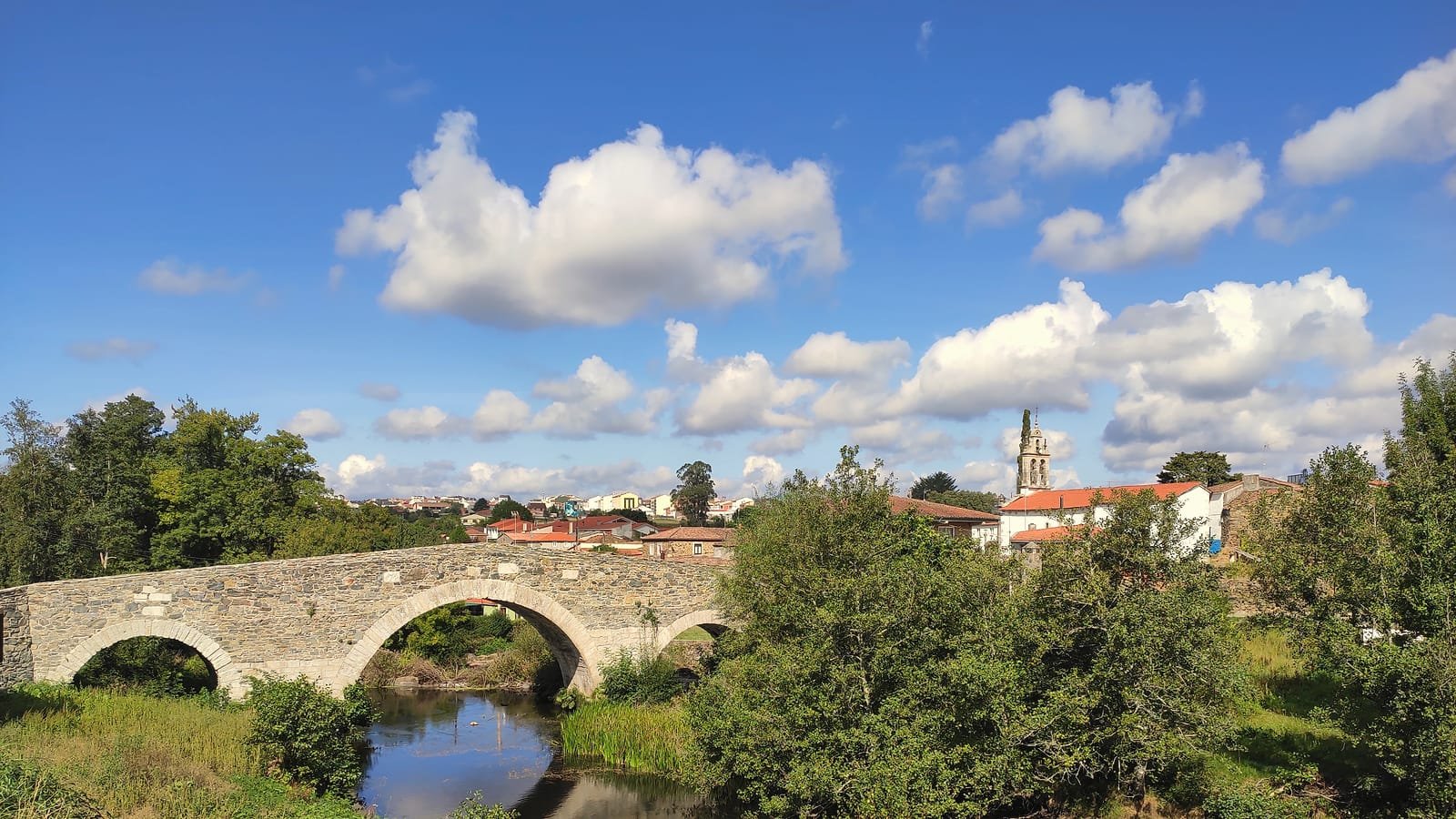 Ponte medieval de Furelos sobre o rio e a aldeia com o campanário, etapa Palas de Rei – Arzúa